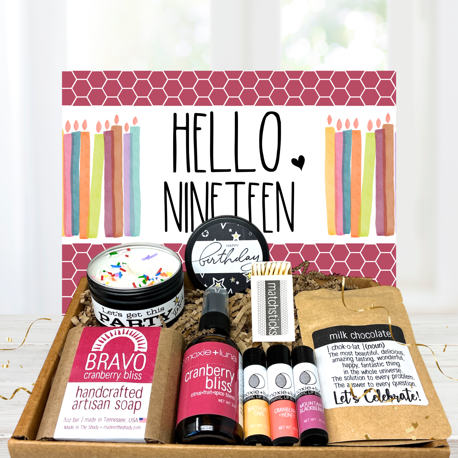 Gift set with products and a decorative card reading 'Hello Nineteen' on a white background.