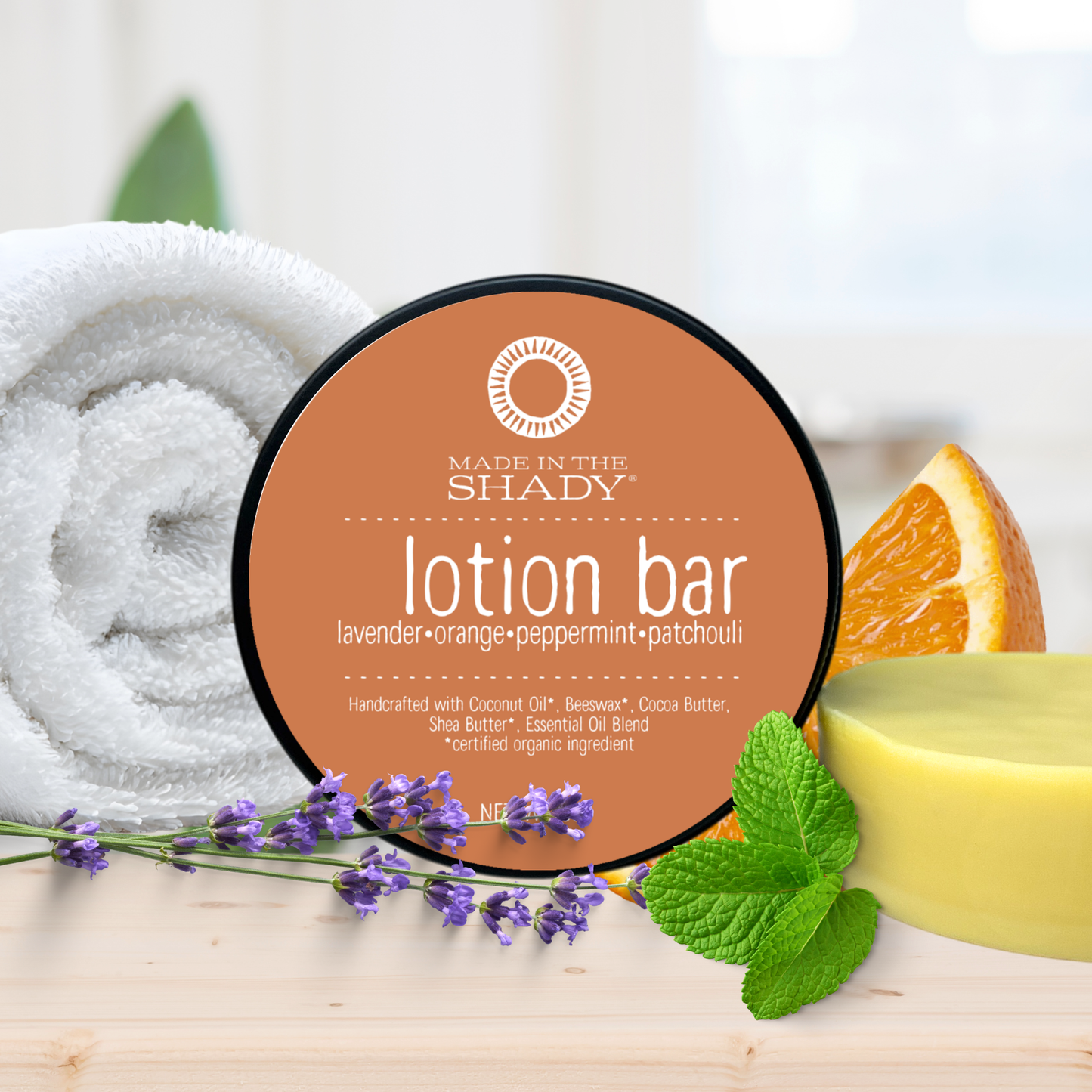 Lotion bar with lavender, orange, peppermint, and patchouli scents on a wooden surface with herbs and an orange slice.