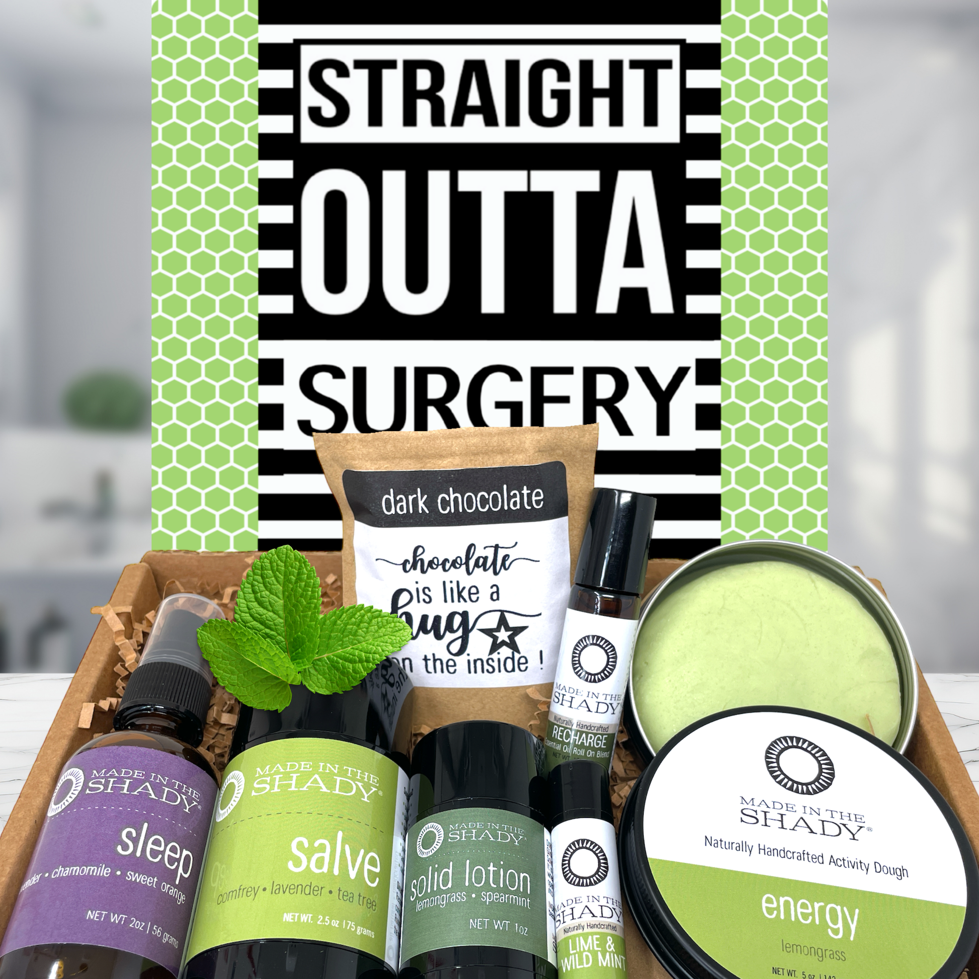 A curated gift box set from Shady Apothecary featuring multiple scented products including sleep spray, herbal salve, solid lotion, energy balm, and a dark chocolate candle, arranged in a gift box in front of a green and black patterned card that reads 'STRAIGHT OUTTA SURGERY'.